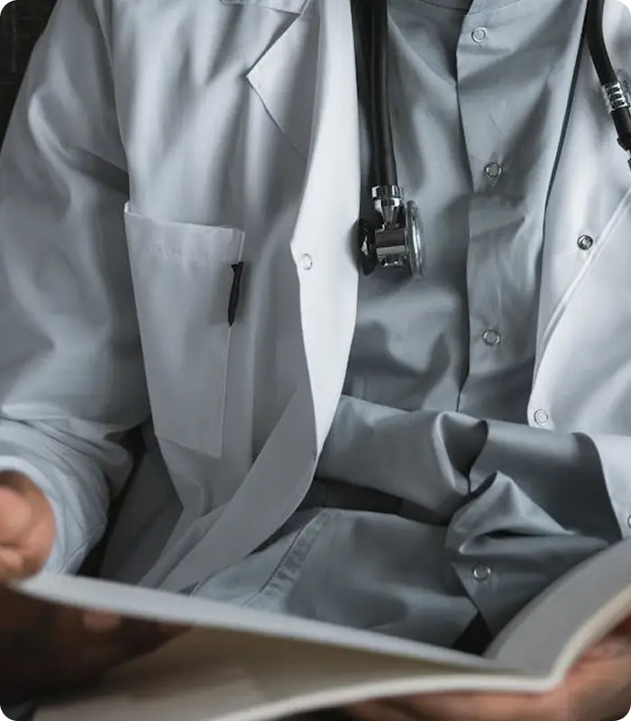 A person wearing a white lab coat and stethoscope reads an open book or document, suggesting an Oncologist in Guildford or testicular cancer specialist reviewing important medical information.